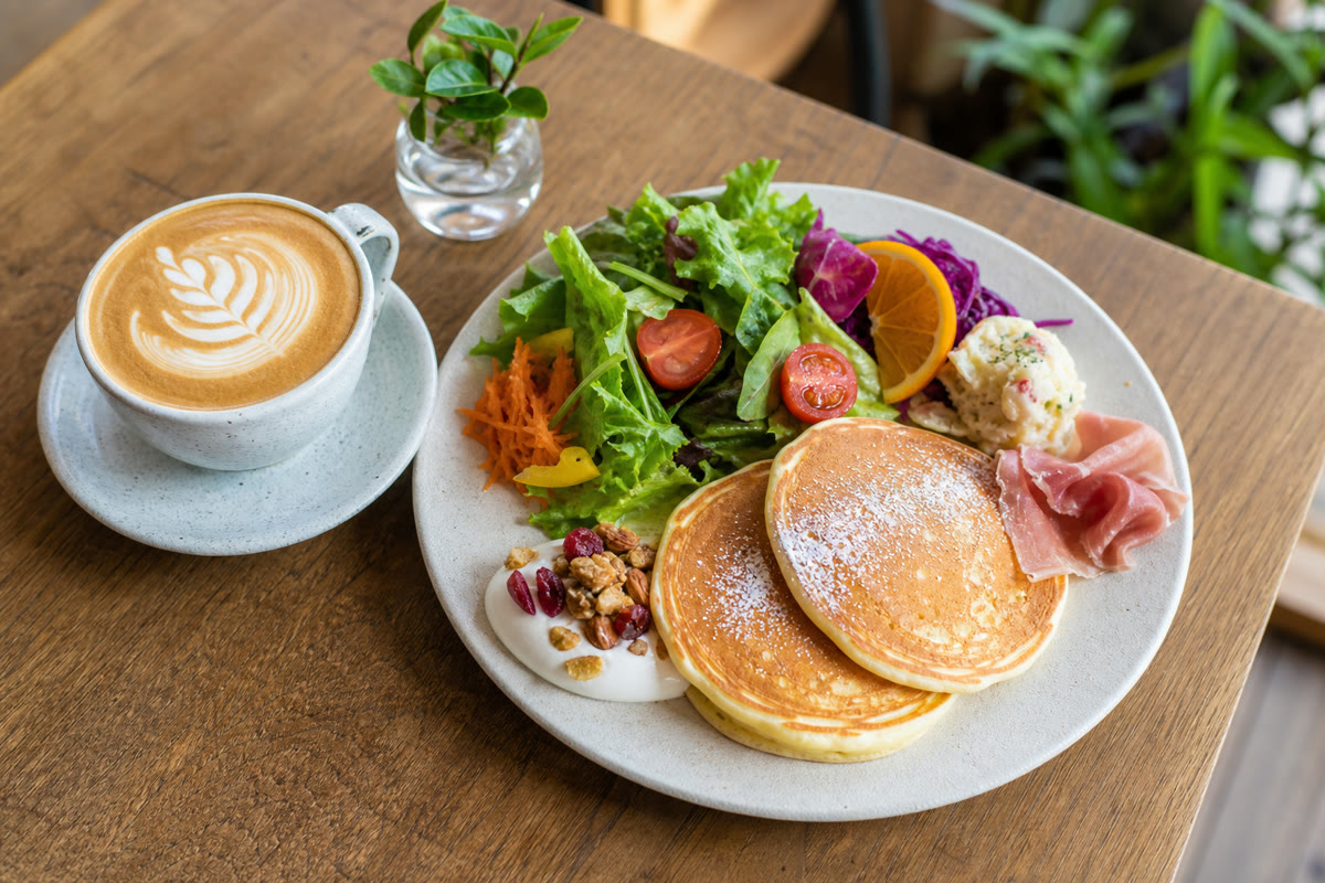 明るい自然光で撮影されたカフェの料理。ラテアートのカフェラテと彩りのよいブランチプレート