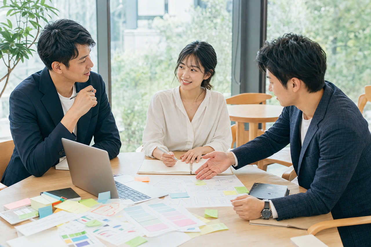 日本人のメンバーが付箋やノートを広げ、明るいテーブルでホームページの戦略を相談している打ち合わせの様子